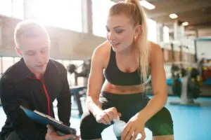Personal trainer chatting and discussing training plan with client during a workout in the gym.