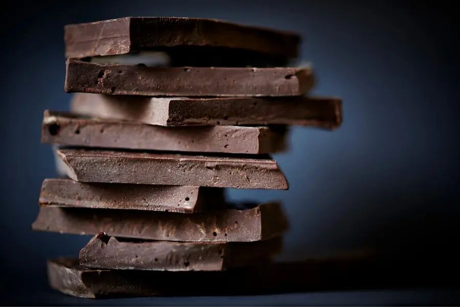 Mood Boosting Foods including dark chocolate stacked in pile with dark blue background