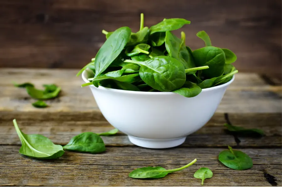 Mood Boosting foods Spinach leaves in a wide dish on a table with some spinach leaves on the table