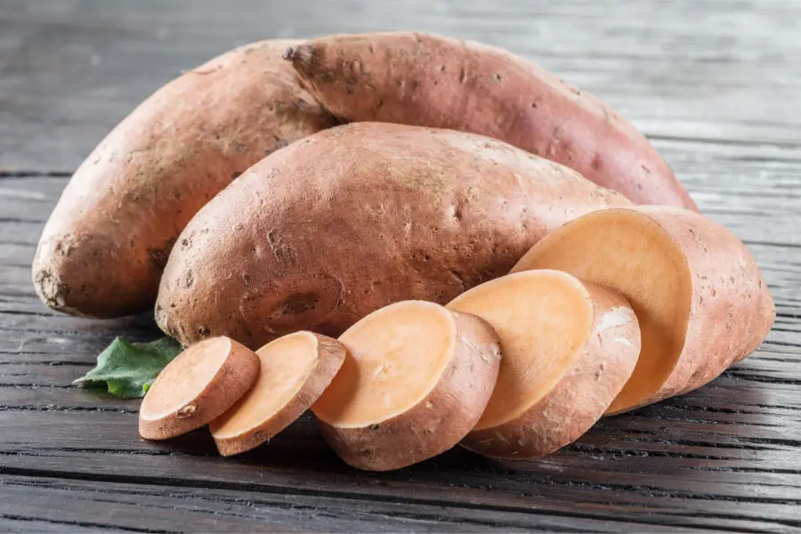 Mood Boosting foods Close up up of 2 uncooked sweet potatoes and one sliced seet potato on brown wooden table