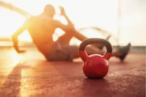 Kettle bell in focus, a man in background doing personal fitness training in the early morning at sunrise.