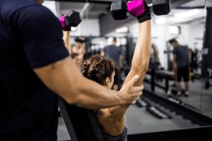 Personal trainer for weight loss and toning working with a young women who is performing seated dumbell press while the personal trainer spots her