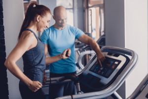 A personal trainer with a slender woman setting her up for a training session on the running machine as part of her training regime to lose weight